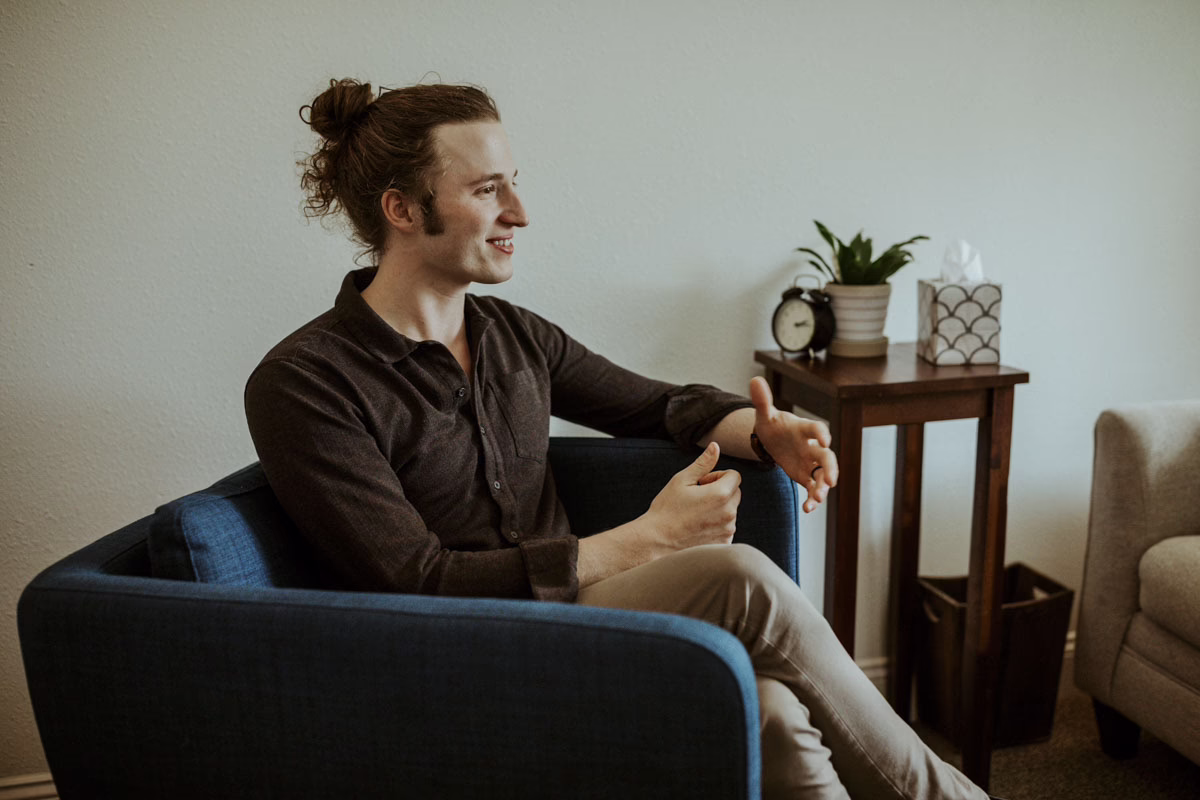 A man smiles while talking in a blue armchair in a Beyond Healing counseling office