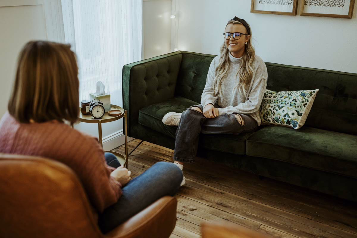 A smiling woman talks from a green velvet sofa in a Beyond Healing office