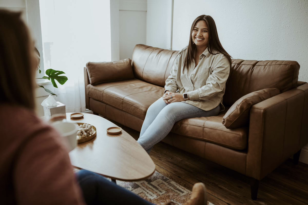 A woman smiles from a leather sofa during a session in a Beyond Healing office