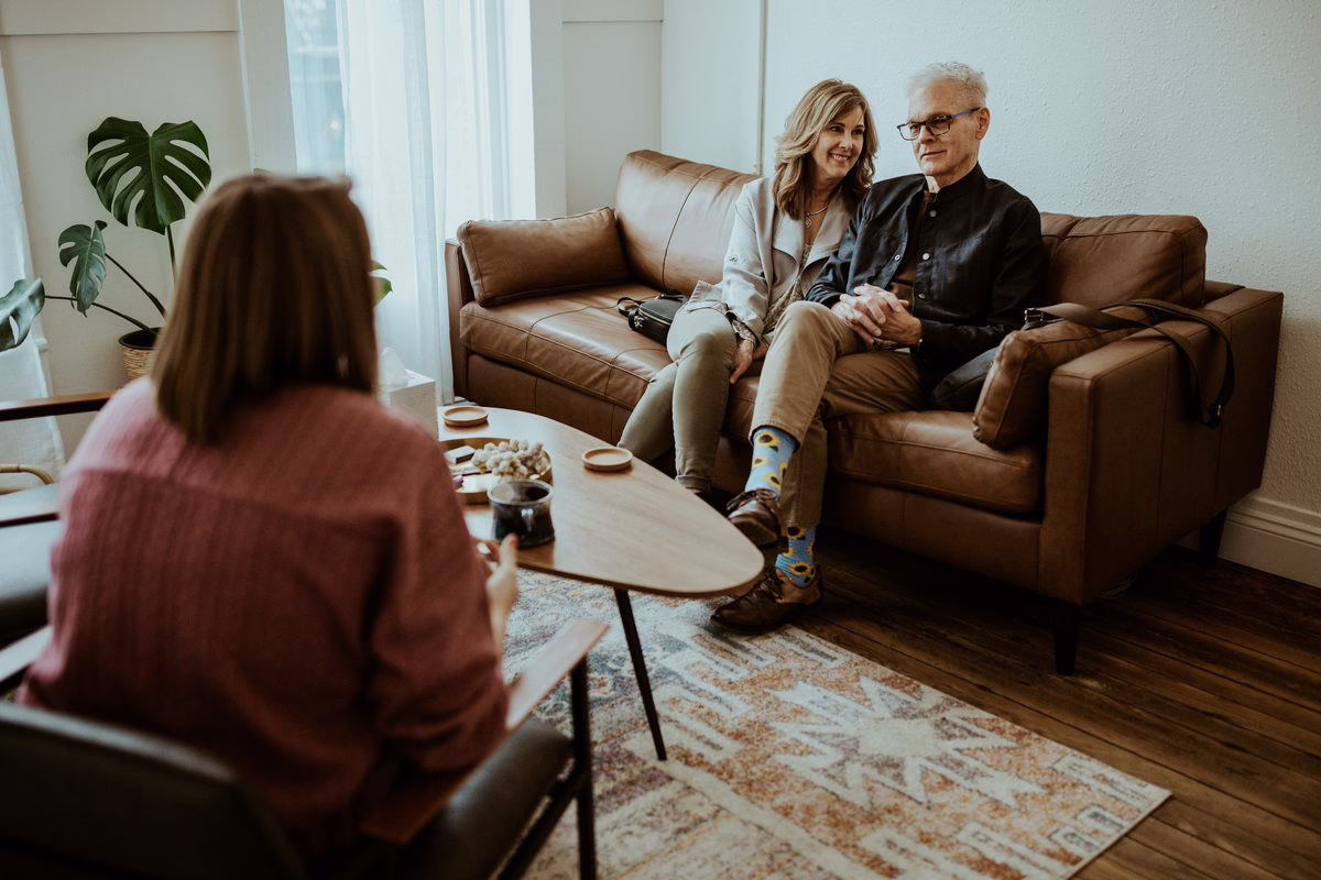 A couple sits together on a leather sofa, talking with a therapist in a Beyond Healing counseling office